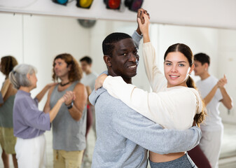 Happy african-american guy and caucasian girl practising paired latin dance in dance studio