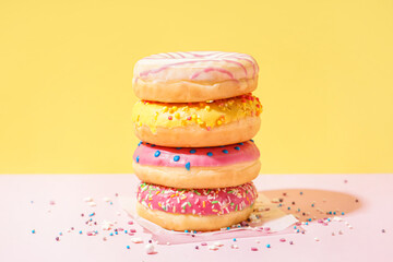 Parchment with different delicious donuts on pink table near yellow wall