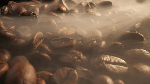 Brown Roasted Coffee Beans With Smoke Closeup On Dark Background. Slider shot of coffee beans during roasting. Smoke comes from fresh coffee seeds. Macro shot, 4K