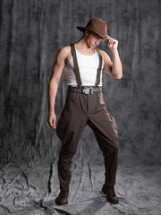 young man in a rural retro style, a character in an adventure western. A guy in a hat and a T-shirt, breeches with suspenders.