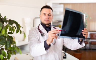 European man physician standing in office and analyzing roentgenogram.