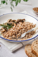 Plate of tasty buckwheat porridge with mushrooms and dill on grey table