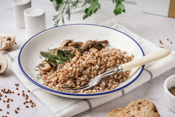 Plate of tasty buckwheat porridge with mushrooms and dill on grey table