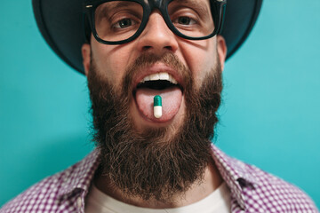 A handsome man in casual clothes with a beard in glasses takes colorful pills. Drug pill on the...