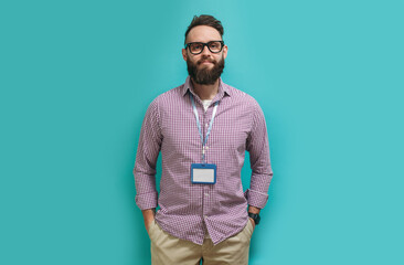 Young caucasian man with a beard in glasses for vision with a blank badge isolated on a blue color...