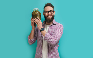 Portrait of a handsome farmer in glasses with a beard holds fresh cucumbers in a jar in his hands....