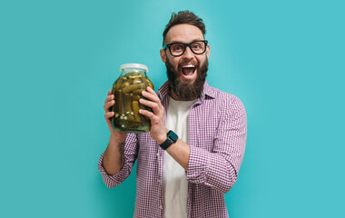 Portrait of a handsome farmer in glasses with a beard holds fresh cucumbers in a jar in his hands....