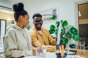 Diverse couple using laptop while sitting at the table at home