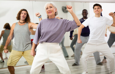 Fototapeta na wymiar Energetic elderly lady attending group choreography class, learning modern dynamic dances. Concept of active lifestyle of older generation..