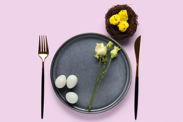 Table setting with Easter eggs, eustoma flowers and baby chickens in nest on lilac background