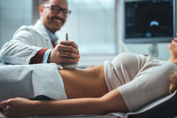 Obraz na płótnie Canvas Mid adult male doctor using ultrasound scanner. Ultrasound exam. Doctor's hands on a woman's stomach, ultrasound of the abdominal cavity, close-up.