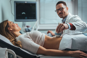 Pregnant woman undergoing ultrasound test at gynecologist office. Closeup of male doctor moving ultrasound probe on pregnant woman's stomach in hospital. Doctor and patient.