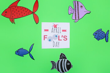 Card with text APRIL FOOL'S DAY and paper fishes on green background