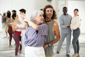 Fototapeta na wymiar Positive elderly woman enjoying dancing in pair with expressive man during group training in dance studio