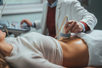 Ultrasound scanner device in hand of professional doctor examining his patient. Expecting pregnancy. Doctor in white lab coat and sterile gloves examining woman with ultrasound scanner