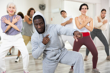 Fototapeta premium Cheerful adult African American man learning to dance krump with group in modern choreographic studio