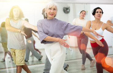 Enthusiastic elderly woman practicing modern vigorous dance movements in group dance class ..