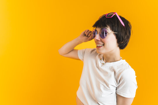 Sunglasses and holiday relaxation concept. Funky short-haired young girl wearing two pairs of sunglasses and looking at copy space. Orange background. High quality photo