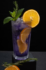 a purple cocktail glass decorated with orange and mint on a dark background