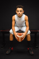 Fototapeta na wymiar Young Youth Preteen Boy Football Player Sitting with Football on Bench in Studio