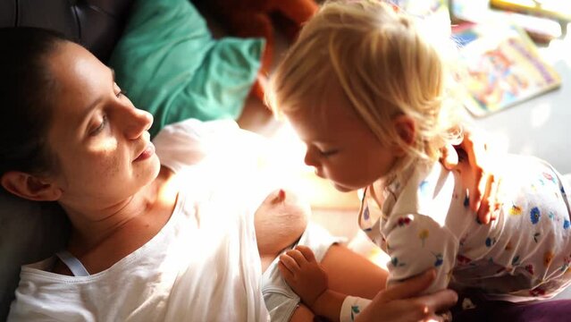 Mom breastfeeds a little girl lying on the bed with her
