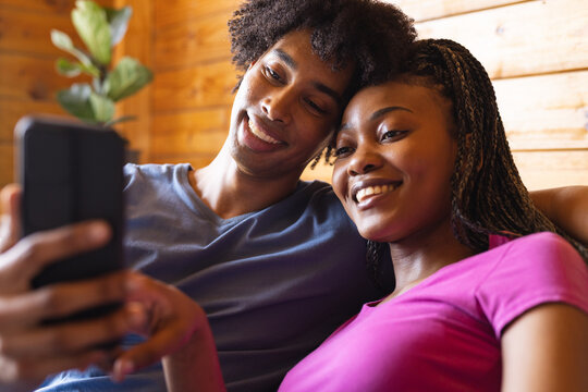 Happy african american couple spending time in log cabin using smartphone
