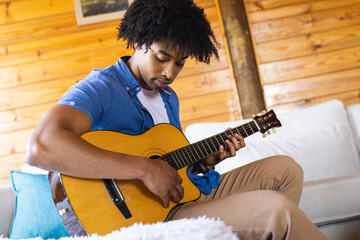 Happy african american man spending time in log cabin playing guitar