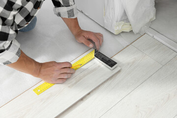 Fototapeta na wymiar Professional worker using measuring tape during installation of laminate flooring, closeup