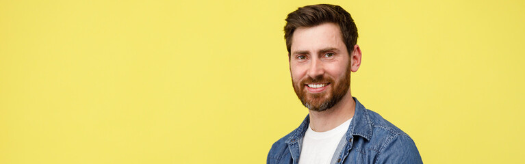 Handsome smiling man with beard holding laptop and looking at camera on yellow background