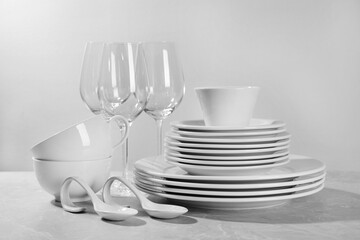 Set of clean dishware and glasses on grey table against light background