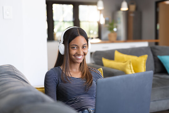 Happy biracial teenage girl wearing headphones and using laptop