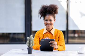 Focused African American biracial woman student with afro hairstyle wear yellow cardigan, have a hot drink and sitting at outside working doing remote job on laptop, 