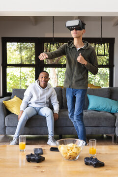 Vertical image of happy diverse male teenage friends with vr glasses playing video games at home