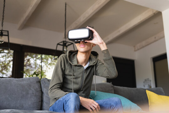Biracial teenage boy with vr headset sitting on sofa at home