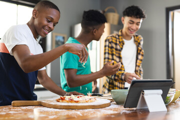 Happy diverse teenage male friends preparing pizza in kitchen