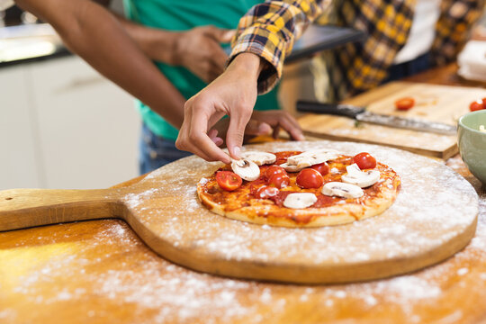 Hands of diverse teenage male friends preparing pizza in kitchen