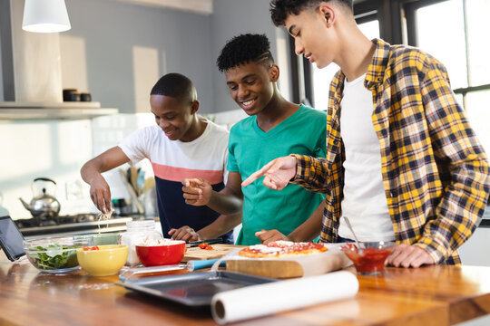 Happy diverse teenage male friends preparing pizza in kitchen