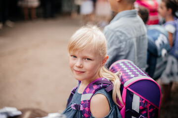 Erstklässlerin mit Rucksack am ersten Schultag, die direkt in die Kamera schaut