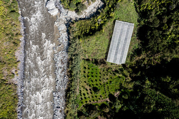 A small greenhouse and a bright green agriculture field located next to a wild mountain river