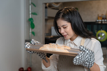 Asian Woman Baker wearing apron and sniffing aroma from bread after baked