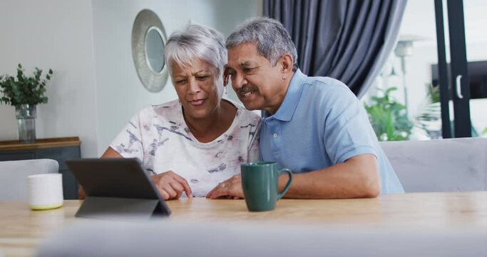 Happy senior biracial couple laughing and using tablet