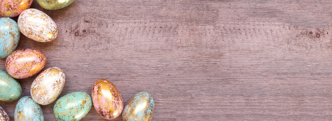 Gold speckled Easter egg corner border. Top down view on a light wood banner background. Copy space.