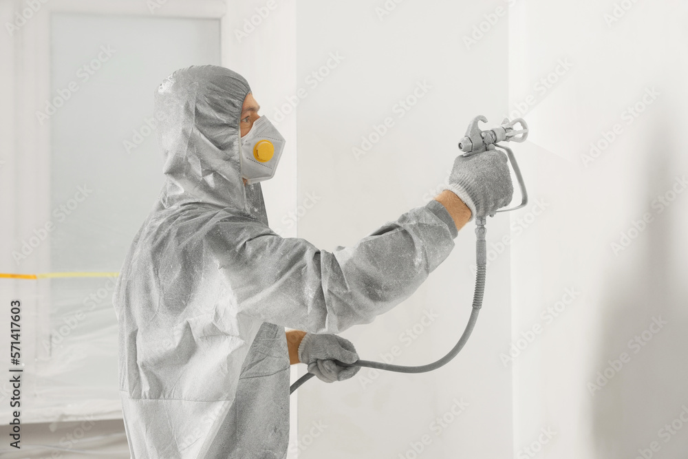 Canvas Prints Decorator in protective overalls painting wall with spray gun indoors