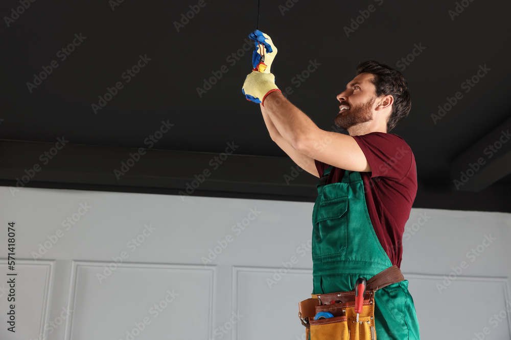 Poster electrician with pliers repairing ceiling wiring indoors