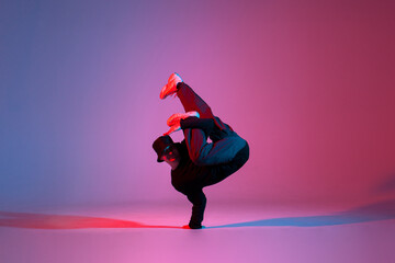 young guy dancer break dancing in neon red blue lighting, active energetic man doing acrobatic...