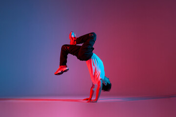young guy dancer break dancing in neon red blue lighting, active energetic man doing acrobatic tricks, crazy moves
