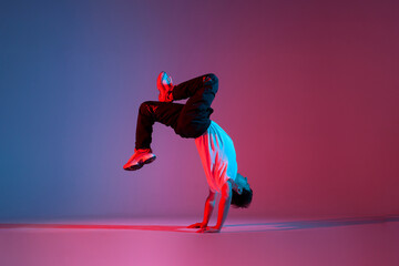 young guy dancer break dancing in neon red blue lighting, active energetic man doing acrobatic...