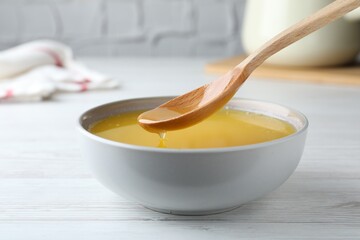 Spoon of clarified butter over bowl on white wooden table