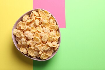 Bowl of tasty crispy corn flakes on color background, top view. Space for text