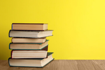 Stack of old hardcover books on wooden table against yellow background, space for text
